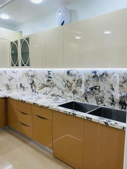 This kitchen features glossy beige handleless cabinets and a stunning, heavily-veined marble countertop and backsplash. The dual sinks are a practical feature for busy households.