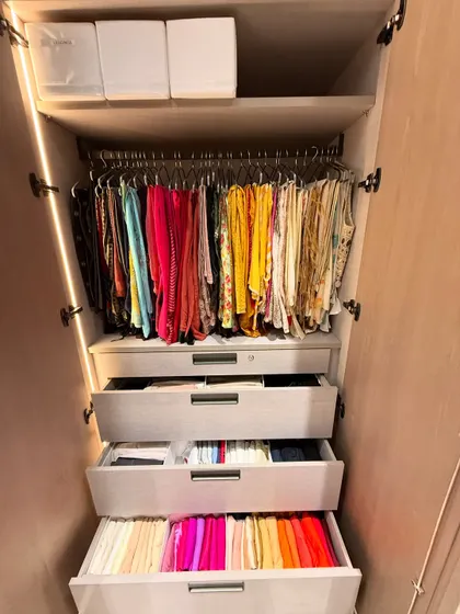 A vibrant collection of dupattas and scarves hanging above drawers filled with color-coded, vertically folded items.