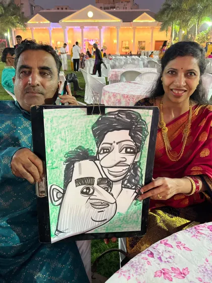 A couple posing with their caricature in the evening, with the beautiful event lighting in the background.