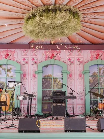A close-up of the stage backdrop, which features a custom-printed floral wallpaper and mint-green arched windows. The central floral chandelier adds a touch of whimsical elegance.