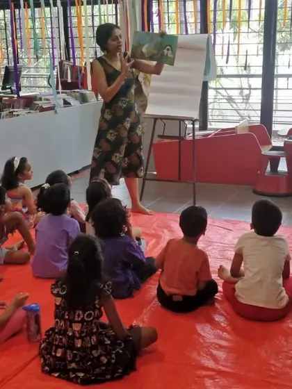 A wide shot of the group listening to Priya Kuriyan, with colorful decorations in the background.