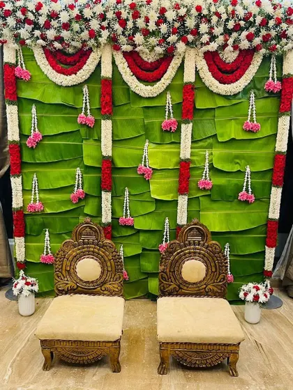 I specialize in creating authentic traditional setups that honor your heritage. This South Indian Pellikuthru decor features a fresh banana leaf wall, intricate garlands of red and white flowers, and ornate wooden seating for the ceremony.