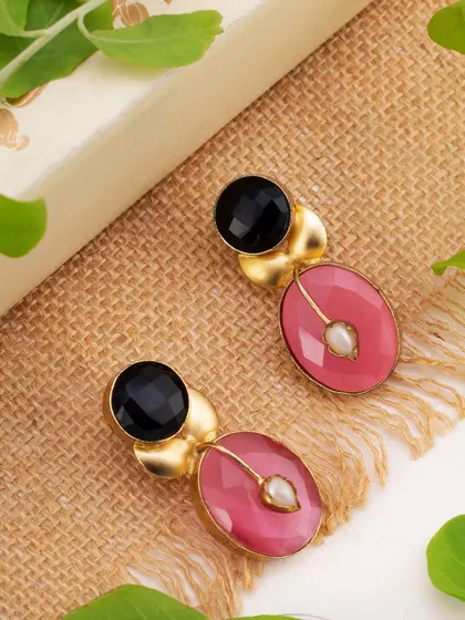A pair of contemporary earrings with pink and black stones, styled on a natural jute surface with green leaves. This composition gives the product an organic, earthy feel, perfect for lifestyle-oriented brands.