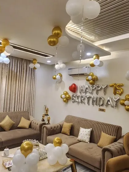 A full living room view of the 75th birthday decoration. The gold and white balloons are tastefully placed to complement the home's modern interior.