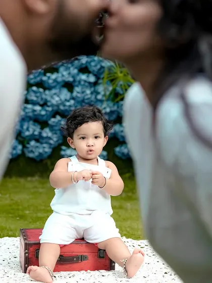A creative and intimate family photo. We focused on the baby's curious expression while his parents share a kiss in the background, creating a beautiful story of love and family.