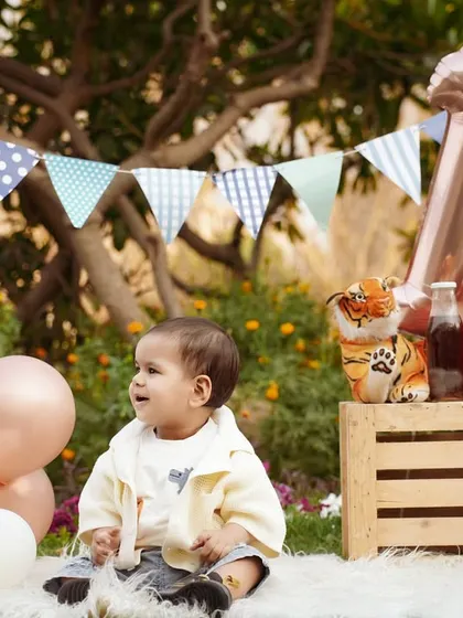 A charming outdoor first birthday picnic. The setup with bunting, balloons, and a crate of juice bottles creates a relaxed and festive vibe.