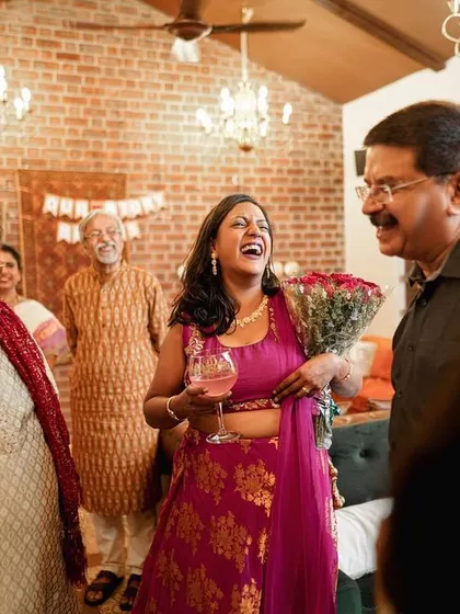 The bride shares a laugh with her family, holding a bouquet of roses during a celebration.