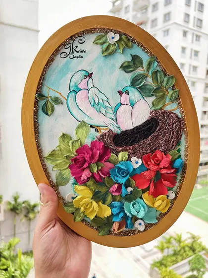 The full view of the oval panel with the two blue birds in their nest. The golden frame and outdoor lighting really make the colors of the flowers and birds pop.