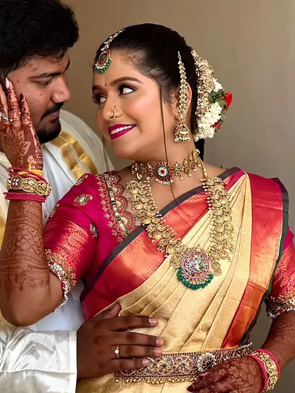 A sweet, candid moment. The bride is wearing a classic temple jewellery set with a beautiful choker and haram that stands out against her cream and pink saree.