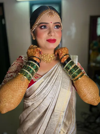 A happy Kannada bride in a traditional white and red saree. Her makeup is fresh and radiant, with a classic red lip and beautifully defined eyes, perfect for her wedding ceremony.