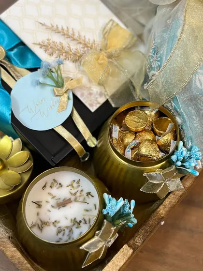 A throwback to a beautiful wedding gift hamper in shades of teal and gold. The tray is filled with a scented candle, a jar of chocolates, and other custom-wrapped goodies.