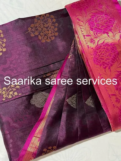 A purple saree with a bright pink floral border. The pleats are set to showcase the beautiful contrast.