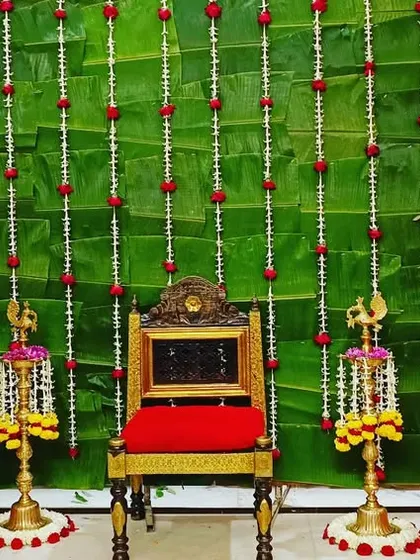 A closer view of the Devkarya puja setup, showing the ornate red chair for the main rituals. The space is framed by baskets of marigolds, hanging floral strings, and traditional brass lamps, creating a truly authentic setting.