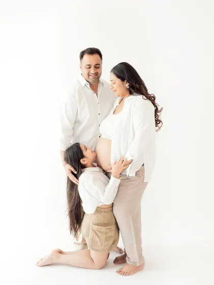 Awaiting the new arrival. A beautiful maternity portrait where the older sister gives a loving kiss to her mother's baby bump, full of anticipation and love.