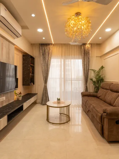 Welcome to the Tawde residence in Pune. The living room is designed with a minimalist approach, using neutral tones, recessed ceiling lights, and a stunning chandelier to create a calm yet luxurious atmosphere.
