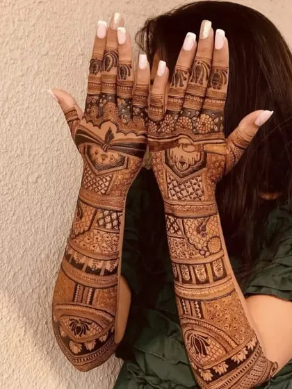 A happy client showing off her full bridal mehndi, which features lotus motifs and detailed patterns up to the elbows.