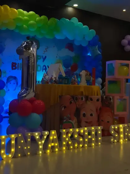 A low-angle shot of the Cocomelon first birthday stage, emphasizing the glowing marquee letters spelling out "PUNYAKSHI SINGH" in front of the setup.