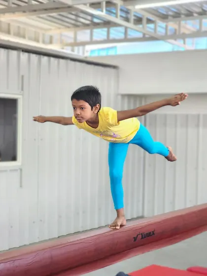 A young student demonstrates excellent balance and posture while practicing a pose on the gymnastics beam.