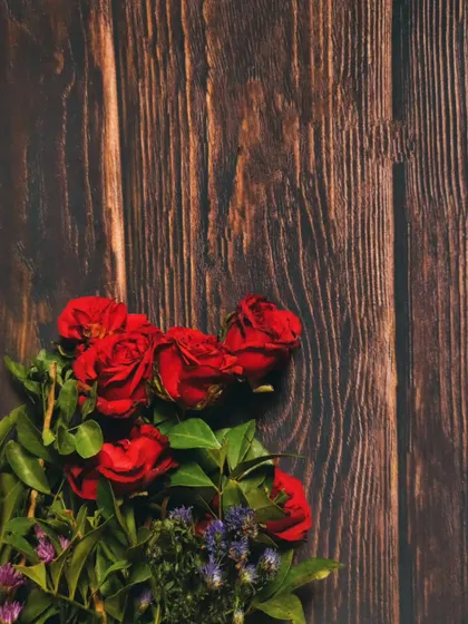A minimalist composition of red roses on a dark wood background, using negative space to create a simple yet elegant image.