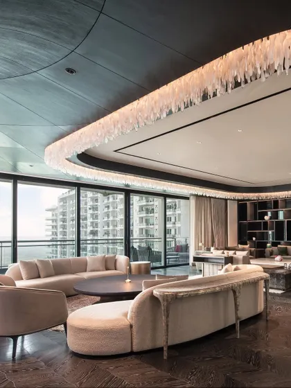 A breathtaking view of a penthouse living room with a curved ceiling and a custom light installation. The organic shapes of the sofas mirror the architecture, creating a space that feels fluid, expansive, and deeply luxurious.