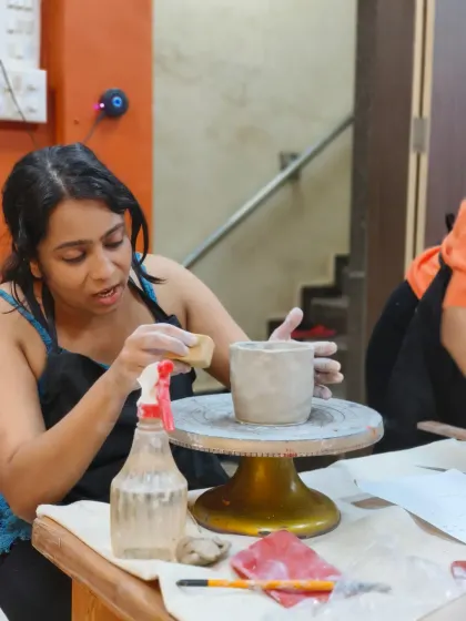 A student uses a sponge to smooth the surface of her white stoneware pot, preparing it for decoration. Proper surface preparation is key to a professional finish.