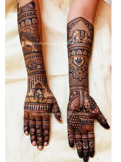 This design tells a story with a bride holding a diya (lamp) on one arm and an elephant in a royal procession on the other. The hands feature swans and peacocks.