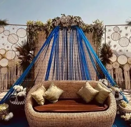 A bohemian-style Mehendi seating area with a wicker sofa and a backdrop of macrame dreamcatchers.