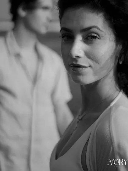 A striking black and white portrait that captures a powerful, direct gaze. The focus is entirely on her expression, with her partner softly blurred in the background, creating a sense of depth and emotional intensity.