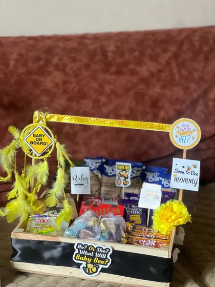 This "What will Baby Bee?" themed hamper is a fun choice for a baby shower. The crate is loaded with chocolates and snacks, and decorated with yellow feathers and bee-themed signs for a unique touch.