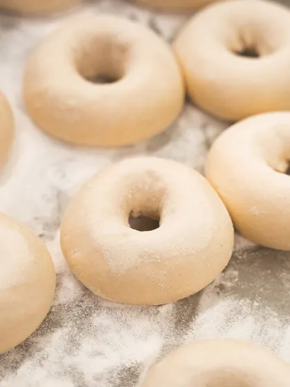 Trays of shaped bagel dough, dusted with flour and ready for their first proof.