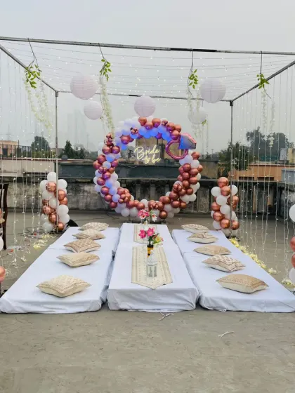 Here’s how I can transform a simple terrace into a chic party space. This bridal shower setup includes a balloon arch with a neon sign, low floor seating with cushions, and a canopy frame with fairy lights and paper lanterns.
