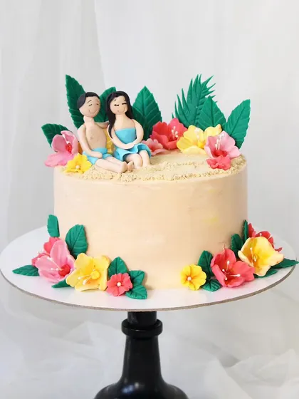 A beautiful beach-themed cake for those who love the sun and sand. This design includes handcrafted fondant figures of a couple relaxing on an edible beach, surrounded by tropical flowers.