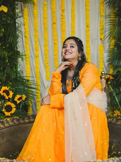 The bride posing against our Haldi decor. The setup includes a backdrop of marigold strings, lush greenery, and sunflowers for a fresh, garden-like feel.