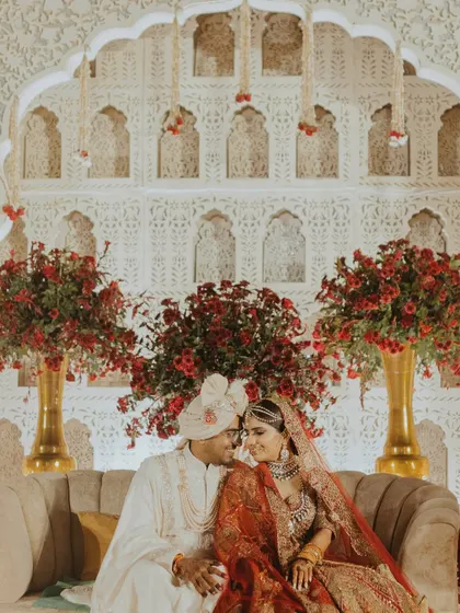 A portrait of the couple seated amidst a backdrop of stunning floral arrangements and intricate architecture, lost in their own world.