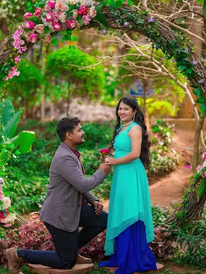 A romantic proposal under a beautiful circular floral arch in a garden.