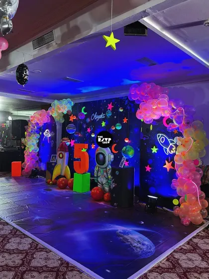 Houston, we have a party! This space-themed neon party stage is out of this world, with a galaxy backdrop, astronaut and rocket props, and a glowing number '5'.