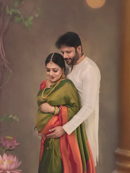 A perfect, timeless portrait capturing the deep connection between a couple. The rich green and orange Kanchivaram saree and traditional jewelry are complemented by the soft, painterly backdrop, creating a frame filled with elegance.