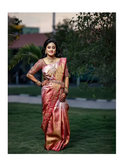 A full-length portrait of the bride in her beautiful pink reception saree, looking elegant and poised in a garden setting.