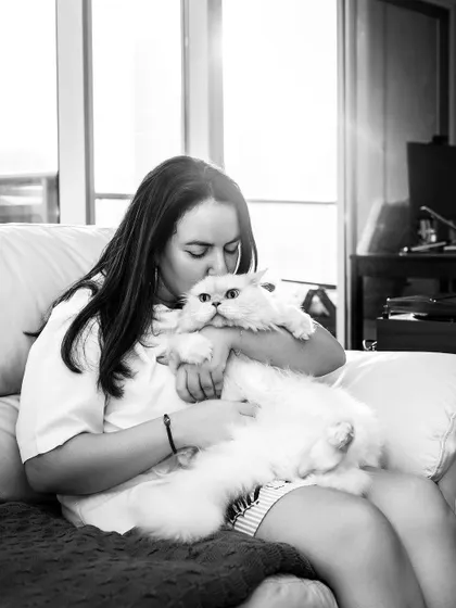 A black and white conversion of a tender moment. A woman gives her fluffy cat a gentle kiss, with the beautiful sunlight streaming in through the window, creating a soft, intimate mood.