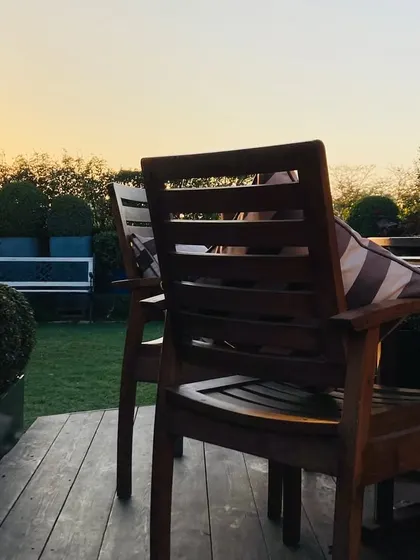 A close up of the wooden deck and chairs on the terrace. The setting sun in the background highlights the peaceful, relaxing atmosphere of this urban garden.