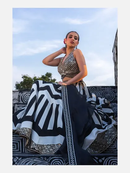 A striking outdoor shot of a model in a modern black and white geometric lehenga by designer Vandana Sethi. The low angle and sky in the background create a powerful and dramatic fashion statement.