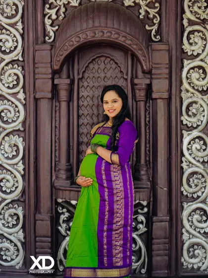 A beautiful solo portrait of the mother-to-be in a green and purple saree, framed by an ornate doorway.