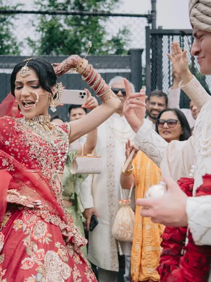 The joy of the baraat! The bride, in her stunning red lehenga, dances with her groom, who is styled in a classic ivory sherwani, creating a timeless and energetic look.