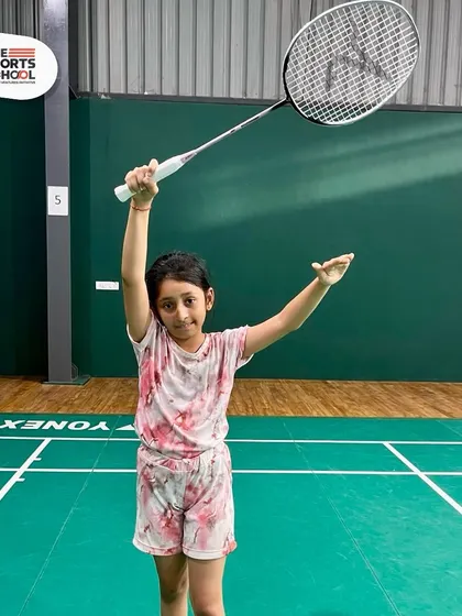 A young girl proudly holds her badminton racket at our summer camp, excited to start her journey in the sport.