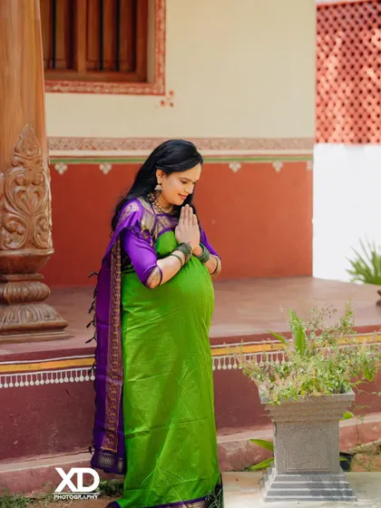A respectful and serene pose of the mother-to-be in a traditional setting, with hands in a prayer-like gesture.