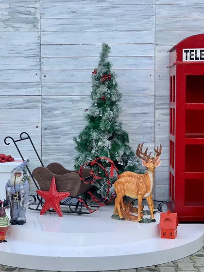 A charming Christmas setup featuring a classic red telephone booth, a sleigh, and other festive elements for a London-inspired holiday theme.
