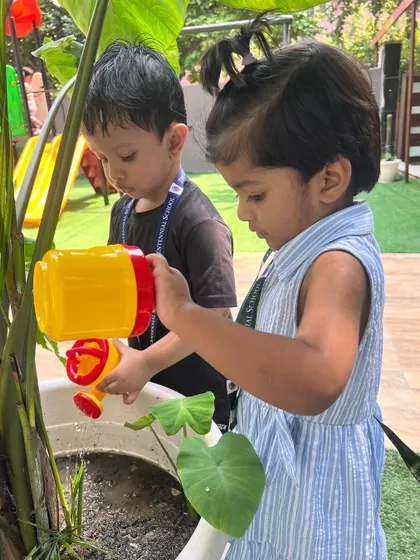 Two children working as a team to water a large plant. These moments of cooperation and shared discovery are what make learning at our school special.