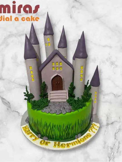 A magical Hogwarts castle cake, perfect for a "Harry or Hermione" gender reveal. The detailed castle sits on a base of green grass frosting, creating a whimsical and mysterious theme.