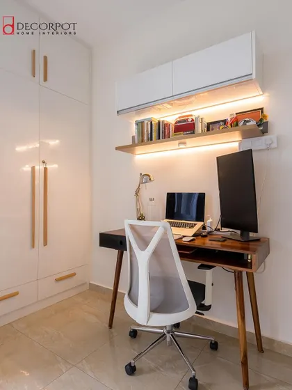 A compact and efficient home office setup. The design features a wooden desk, a comfortable chair, and a sleek white wardrobe, showing how a workspace can be seamlessly integrated into a bedroom.
