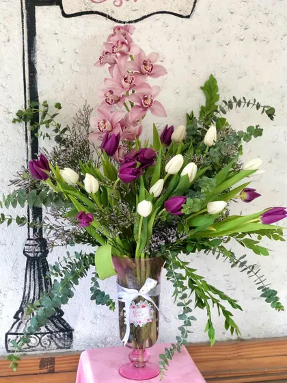 This elegant vase arrangement showcases a beautiful combination of textures and colors. I've paired delicate pink orchids with bold purple and white tulips, accented with fresh eucalyptus leaves for a modern and sophisticated look that feels both fresh and timeless.